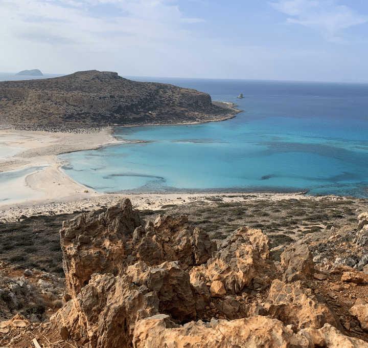 Balos beach from the cliffside, blue water, white sand, headland in the distance